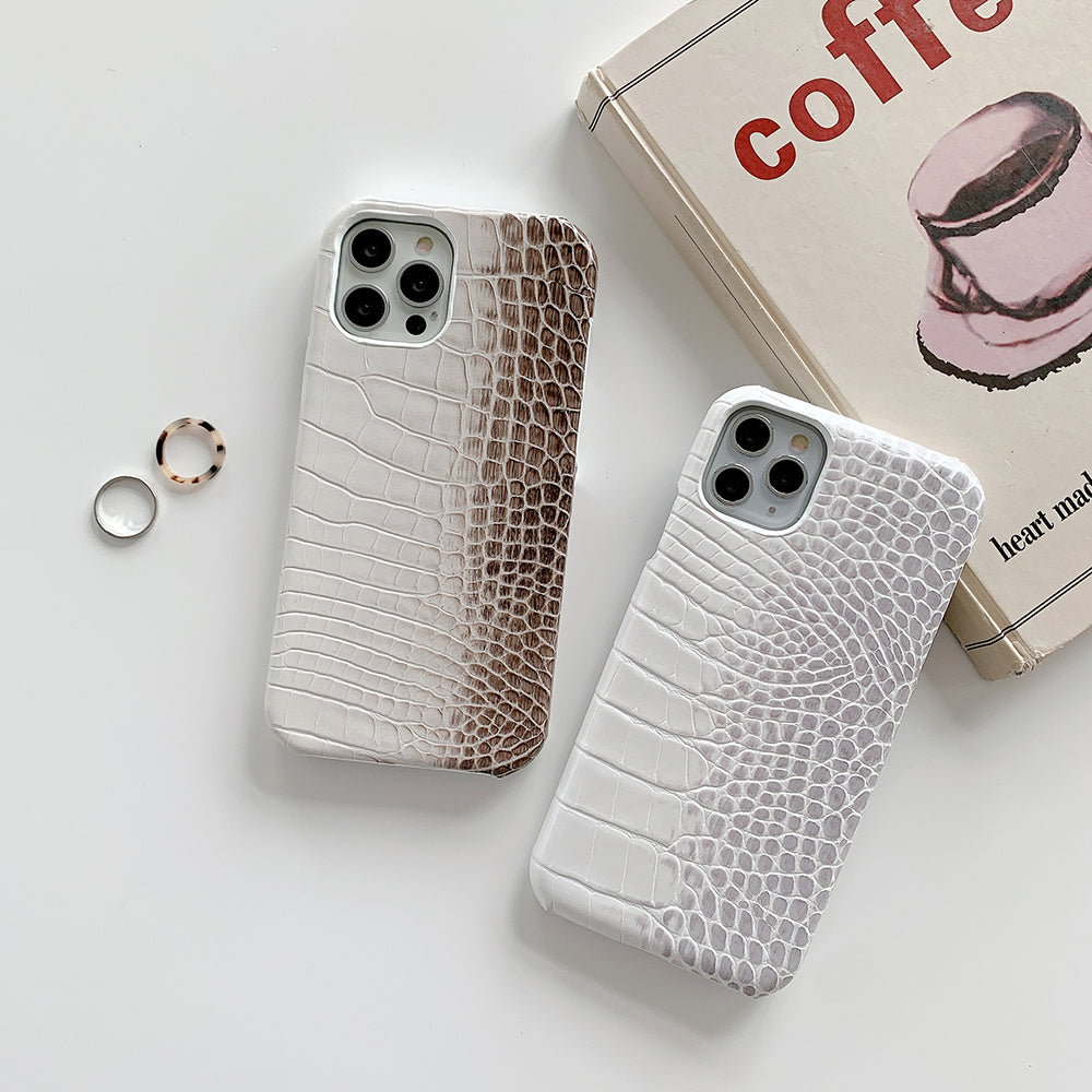 Deux coques téléphone cuir crocodile en dégradé marron et blanc posées à côté d'un livre et deux bagues